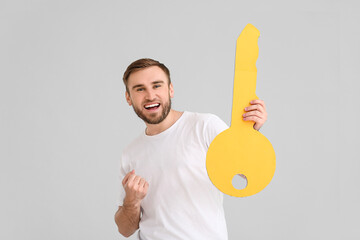 Wall Mural - Happy young man with big paper key on grey background