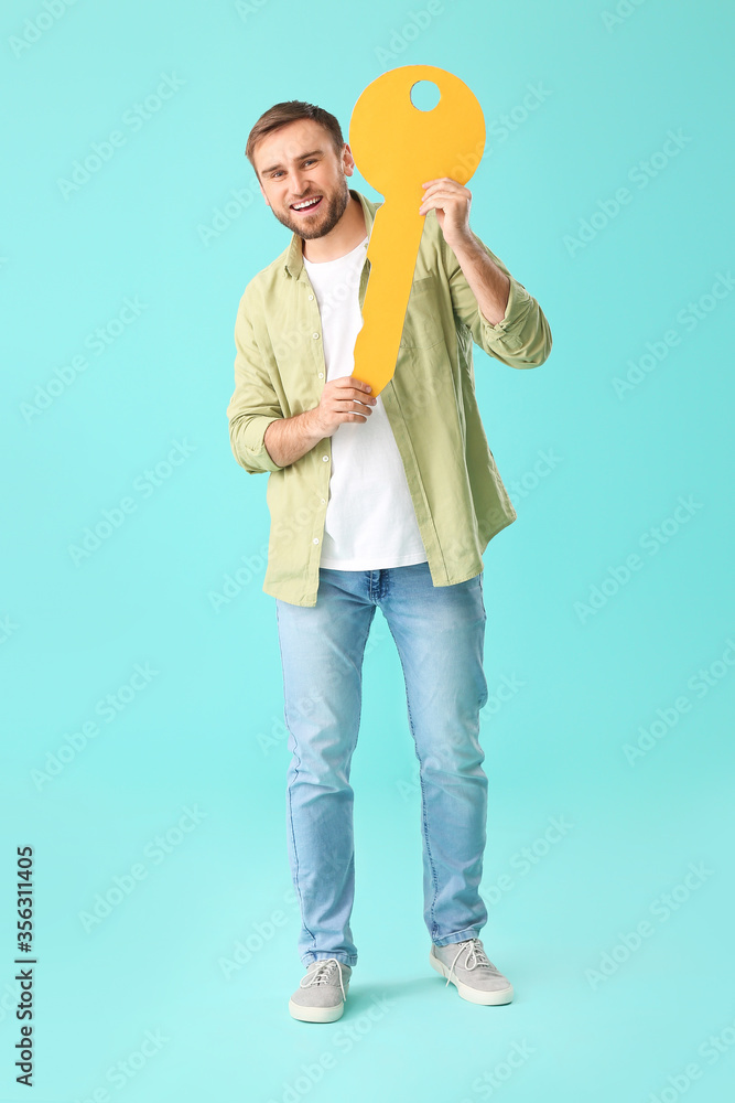 Happy young man with big paper key on color background