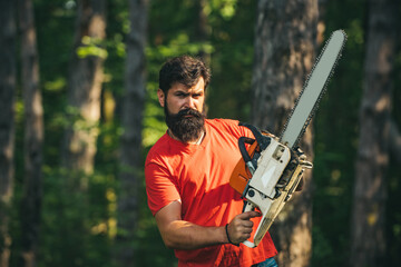 Handsome young man with axe near forest. Deforestation. Lumberjack in the woods with chainsaw axe. Agriculture and forestry theme.