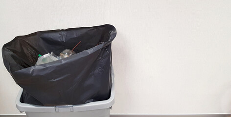 Black plastic bag containing full garbage in gray or grey trash isolated on white wall background with copy space on right. Keep cleaning and Take care environmental or ecology concept 