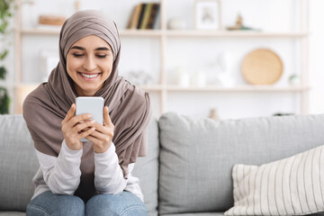 Sticker - Cheerful Muslim Girl In Headscarf Spending Time At Home With Smartphone