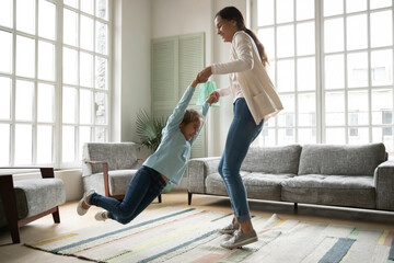 Wall Mural - Happy young Caucasian mother have fun dance swirl or sway with excited little daughter in living room, smiling mom or nanny have fun play together with overjoyed small girl child on weekend at home