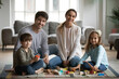 © fizkes - Portrait of happy young Caucasian family with little children sit on warm floor in living room playing toys together, smiling parents have fun engaged in game activity with small preschooler kids