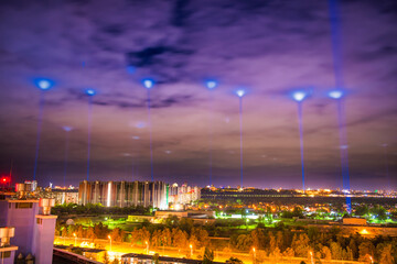 Canvas Print - Night illuminated city with blue lights in the clouds and sky