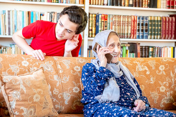 Wall Mural - Happy arabic muslim grand mother and her son sitting together on sofa and using mobiles