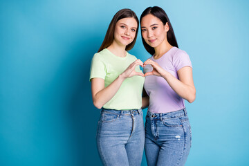 Photo of two affection lesbians couple young students ladies romance date make arms fingers heart shape lovers anniversary wear casual t-shirts jean isolated blue color background