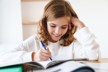 Wall Mural - Photo of happy girl writing in exercise book while doing homework