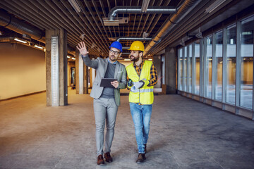 Sticker - Dedicated innovative architect holding tablet and explaining his ideas to construction worker. Building in construction process interior.