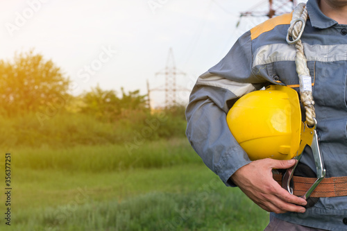 Fotomural A young electrical engineer, with a protective helmet in his hands, against the background of a power line