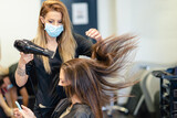 Hairdresser drying her client's hair with a hairdryer wearing protective masks in a beauty centre.