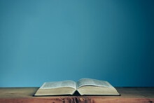 Open Holly Bible On A Red Wooden Table. Beautiful Blue Wall Background. Religious Concept.