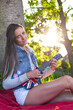 © Andrei KOSCINA - Yung woman playing ukelele in London under a tree