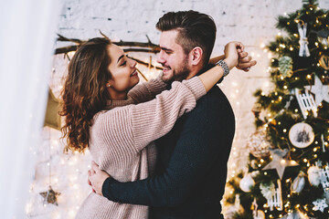 Happy caucasian couple in love having fun together near beautiful Christmas tree 