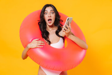 Wall Mural - Image of surprised young woman with rubber ring holding mobile phone