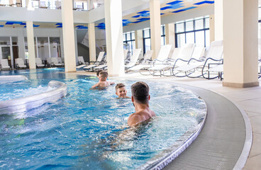 Wall Mural - smiling family of four having fun and relaxing in indoor swimming pool at hotel resort.