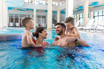 Wall Mural - smiling family of four having fun and relaxing in indoor swimming pool at hotel resort.