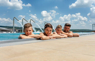 Wall Mural - portrait of smiling family of four having fun and relaxing in outdoor swimming pool at hotel resort.