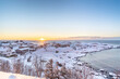 Sunrise from the sea in snowy quiet village in the north. The town covered with white fluffy snow in the beautiful winter while the blight red orange sun rising from the horizon under clear blue sky. 