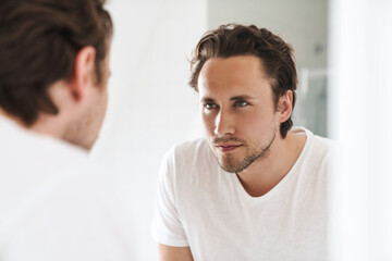 Wall Mural - Attractive young man standing in front of the bathroom mirror