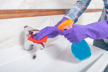 Cleaning in the bathroom. A woman wipes the sink and washbasin faucet.