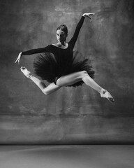 Wall Mural - Balanced. Graceful classic ballerina dancing, posing isolated on dark studio background. Elegance black tutu. Grace, movement, action and motion concept. Looks weightless, flexible. Fashionable.