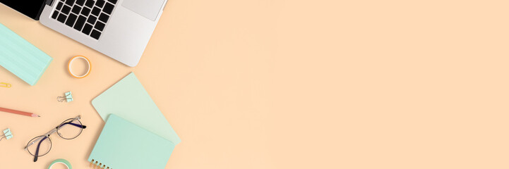 Top view of laptop, glasses and stationery on a yellow pastel background. Workspace concept banner with place for text.