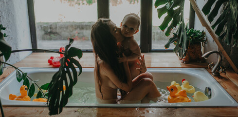 Mother hugs and kisses her baby while bathing in bathtub.