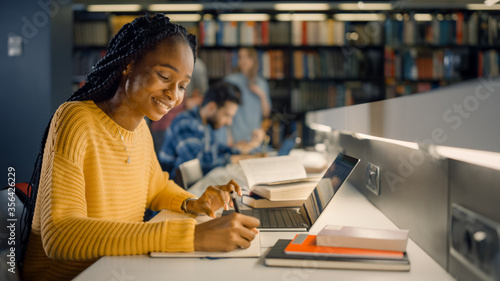 Fotografía University Library: Gifted Black Girl uses Laptop, Writes Notes for the Paper, Essay, Study for Class Assignment