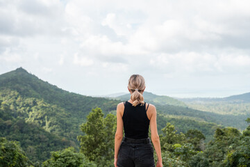 Back side of woman in black t-shirt enjoying tropical forest view with mangrove trees. Mountains and white clouds on a blue sky. Tropical summer holiday vacation concept.