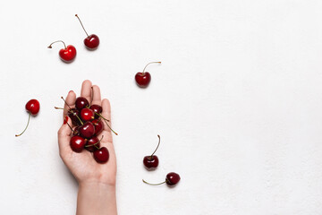 Wall Mural - Female hand holds ripe cherries on white table. Summer background