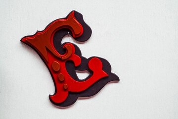 Classic ornate red capital letter wooden E hanging on a plain white wall at an angle.