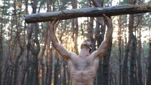 Muscular Man Lifting Hard Weight Over Head Training Hands. Strong Guy With Naked Torso Working Out In Forest. Athlete Exercising At Beautiful Nature Environment. Sport And Active Lifestyle. Dolly Shot