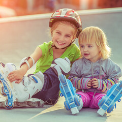 Wall Mural - Cute little sisters in a roller skates sitting on the street