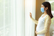 Young pregnant asian woman in medical mask stay alone at home for self quarantine. home quarantine, prevention covid 19, coronavirus outbreak situation concept Pregnancy mother looking through window 