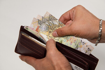 Men's hands holding wallet with Qatari notes. 100 Rial new notes. Financial Concept