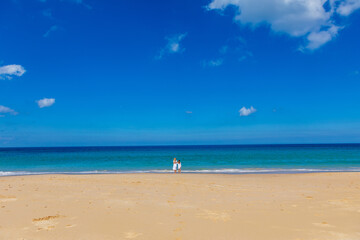 Wall Mural - Young beautiful mother with her charming daughter in white clothes walk on a sandy beach near the water