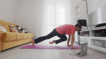 Androgynous Transgender beautiful young gay man with make updoing sports exercises rock climber at home. On-line home work out man using internet services with help of her instructor on laptop