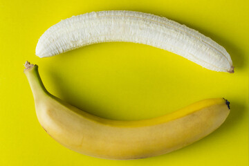 Two bananas on a yellow background. One banana peeled. Photo from above. Banana as background