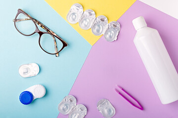 Contact lens kit with bottle of lens solution, case, tweezer on multicolor background, copy space, top view