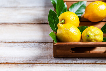 Ripe yellow lemons with leaves in wooden box. Ingredients for refreshing summer beverage - homemade lemonade. Close up, macro view. Wooden rustic background. Copy space for text