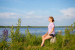 © Ольга Холявина - The concept of walks alone. Young girl with short hair in purple T-shirt and shorts sits on river bank. Summer sunny evening. Copyspace. Cozy cute rural landscape.
