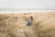 © Milou Dirks - Girl in classic blue dress sitting and contemplating in grass dunes near ocean