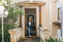 Trendy Modern Woman In Jacket And Light Denim Looking Away While Walking On Porch Of Old House