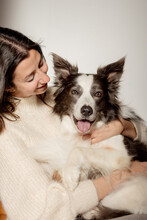 Caring Female In Woolen Sweater Hugging Funny Border Collie Dog While Sitting On Wooden Floor Together