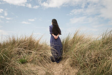 Classic Portrait Of Girl In Vintage Blue Dress Standing In Dunes Seen From Back