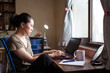 © Juan Alberto Ruiz/ADDICTIVE STOCK - Side view of Asian female freelancer in casual t shirt and eyeglasses sitting at table and browsing computer while working on project online at home