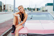 © Manuel Ruiz Alba/ADDICTIVE STOCK - Attractive blonde girl sitting on the hood of a classic pink car on the street