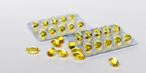 Yellow transparent pills in clear plastic blisters and several capsules are on the table on white background. Selective focus. Medical concept.