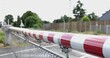 Selected focus view at red and white level crossing railway barrier which block the road until it was lifted, blur background of locomotive move on the rail on countryside.