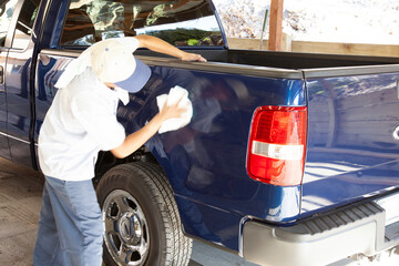 Man bent over polishing side of blue truck as a final detail after collision repair